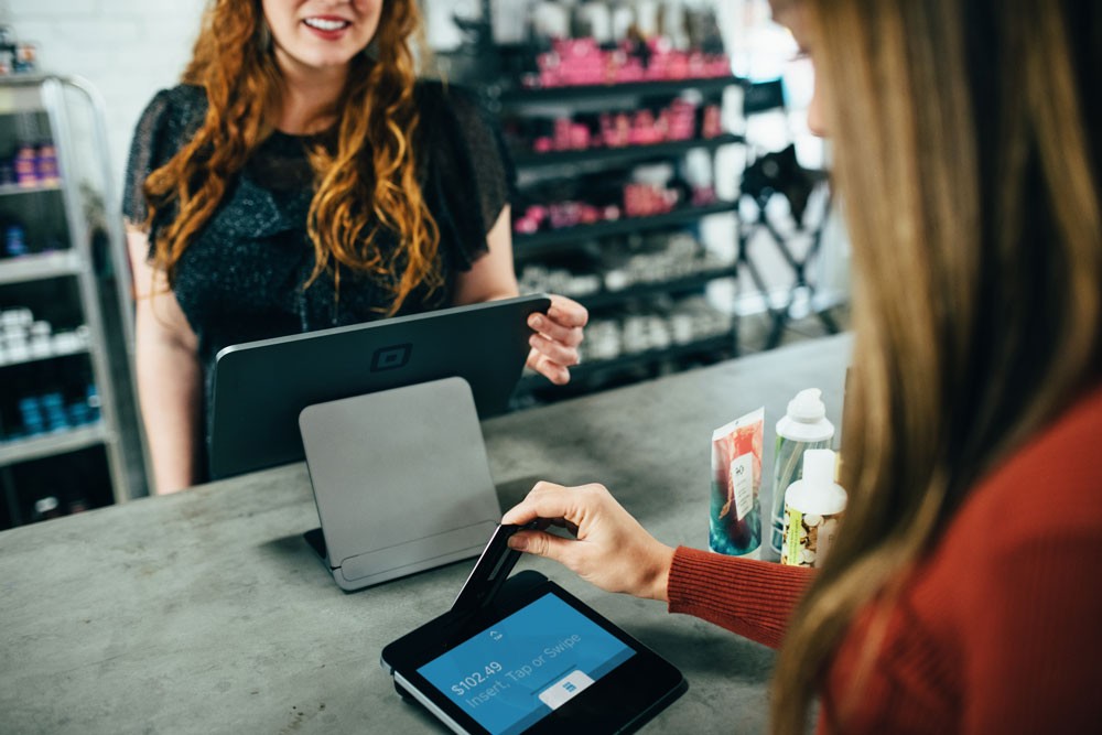 un cliente y la vendedora en el mostrador con el ordenador y la tablet